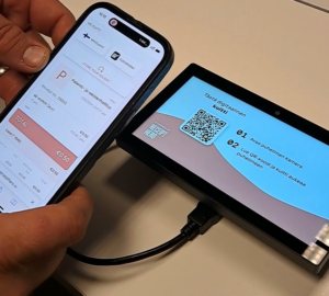 Henkilö lukee mobiililaiteella maksupäätteeltä QR-koodin, ja kuitti ostoksesta näkyy hänen mobiililaitteellaan.